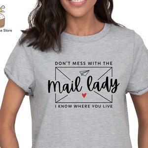 May include: Gray t-shirt with a black graphic that says "Don't mess with the mail lady I know where you live". The graphic is in the shape of an envelope with a paper airplane inside.
