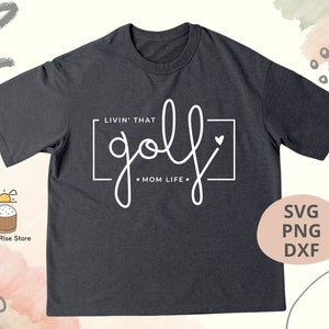 May include: A dark gray t-shirt with the text "LIVIN' THAT golf &bull; MOM LIFE." in white. The text is in a handwritten style with a heart symbol.