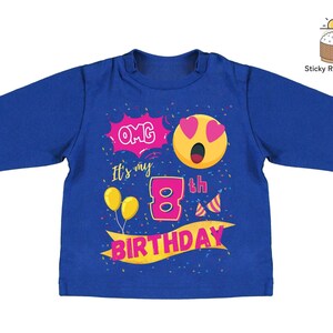 K&ouml;nnte beinhalten: Blaues Langarmshirt mit einem pinkfarbenen und gelben Aufdruck, auf dem "OMG it's my 8th Birthday" steht, sowie einem gelben Smiley mit pinkfarbenen Herzen als Augen.