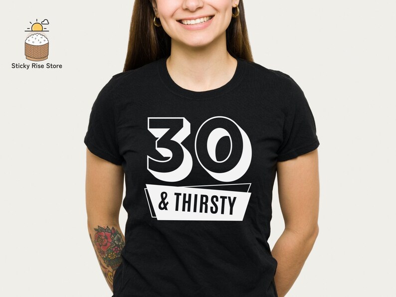 May include: Black crew neck t-shirt with the text "30 & THIRSTY" in white block letters. The number 30 is large and bold, with the words "& THIRSTY" on a white banner below. The shirt is worn by a person.