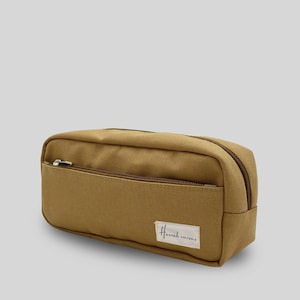May include: A brown canvas pencil case with a zipper closure and a small pocket on the front. The case has a label that says "Homespun Canvas".