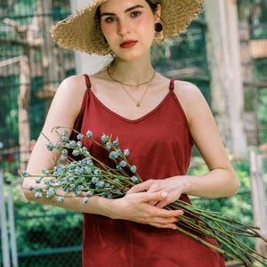 May include: A woman wearing a wide-brimmed straw hat and a burgundy tank top holds a bouquet of dried flowers.