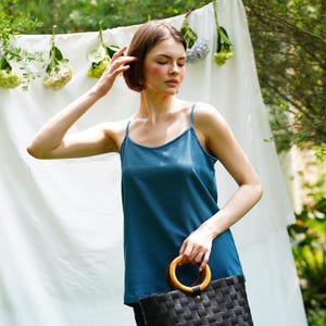 May include: A woman wearing a teal blue sleeveless top with a woven black bag with a wooden handle.