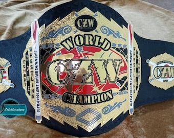 May include: A black leather wrestling championship belt with gold accents. The belt features a large, red, white, and blue logo with the letters "CZW" in the center. The belt also has the words "World Champion" and "Ultraviolent Entertainment" written on it.