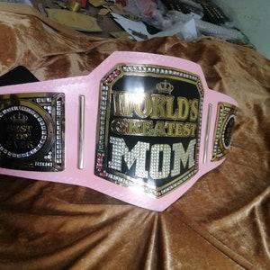 May include: A pink and gold championship belt with rhinestones and the words "World's Greatest Mom" on the front. The belt also has a smaller plate with the words "Best Mom Ever" on it.