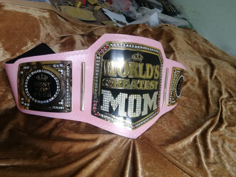 May include: A pink and gold championship belt with rhinestones and the words "World's Greatest Mom" on the front. The belt also has a smaller plate with the words "Best Mom Ever" on it.