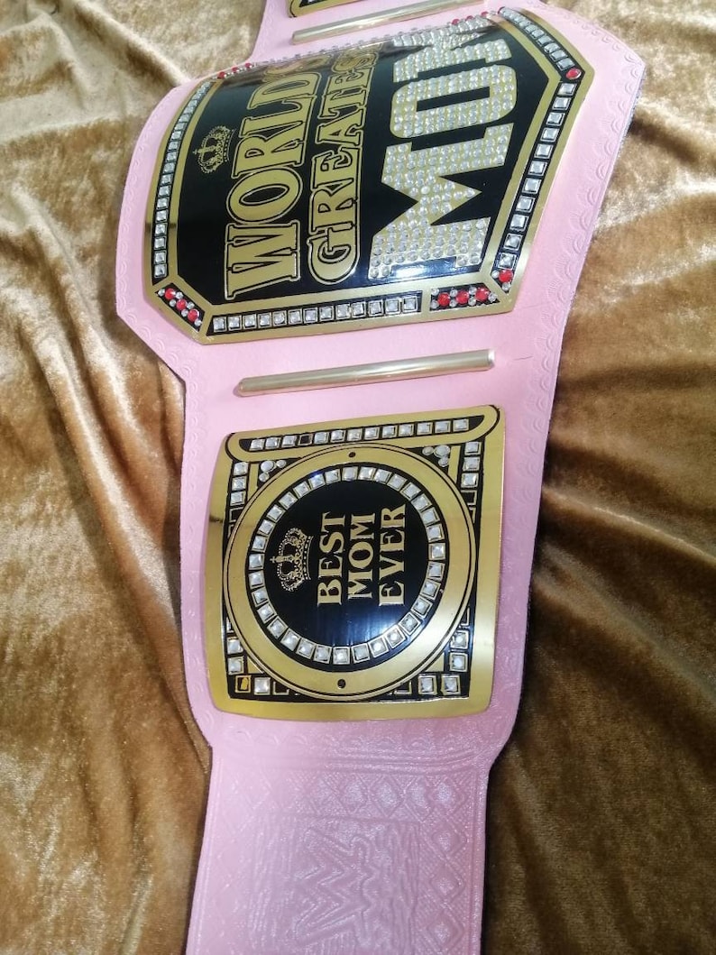 May include: Pink and gold championship belt with rhinestones. The belt has two plates. The top plate says "World's Greatest Mom" and the bottom plate says "Best Mom Ever".