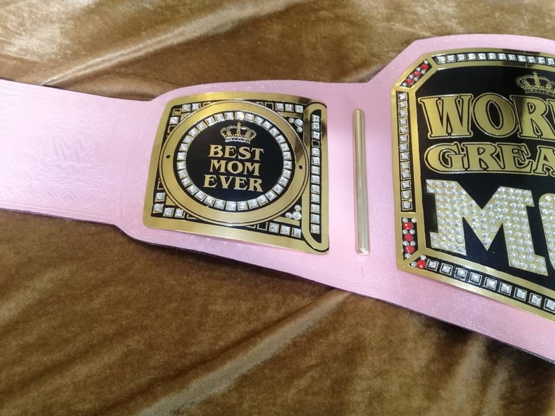 May include: Pink and gold championship belt with rhinestones and the text "World's Greatest Mom" and a smaller plaque with the text "Best Mom Ever" and a crown.