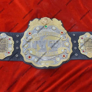 K&ouml;nnte beinhalten: Ein schwarzer Leder-Wrestling-Champion-G&uuml;rtel mit goldenen und silbernen Akzenten. Die Mittelplatte zeigt den Text "International Wrestling Federation" und "IWF" in einer stilisierten Schriftart. Der G&uuml;rtel hat vier Seitenplatten mit goldenen und silbernen Akzenten.