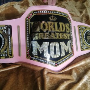 May include: Pink and gold championship belt with rhinestones and the text "World's Greatest Mom" on the front. The belt also has two smaller plates with the text "Best Mom Ever" on each.