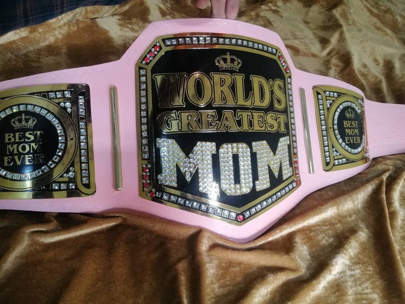 May include: Pink and gold championship belt with rhinestones and the text "World's Greatest Mom" on the front. The belt also has two smaller plates with the text "Best Mom Ever" on each.