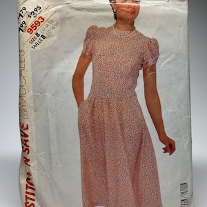 Könnte beinhalten: Ein Vintage-Schnittmuster von McCall's für ein Kleid, Größe B (12-14-16). Das Schnittmuster ist für ein Kleid mit rundem Ausschnitt, kurzen Ärmeln und einem gerafften Rock. Das Schnittmuster ist auf weißem Hintergrund mit schwarzem Text gedruckt.