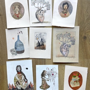 May include: A collection of eight rectangular art prints featuring watercolour and ink illustrations of human figures, anatomical hearts with tree branches, a vase with a skull, and a bird-headed figure, all with the text Vide atelier 15 euros pièce.