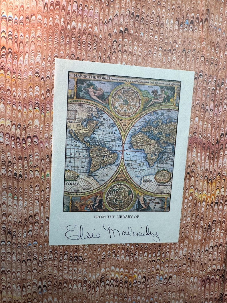 May include: A vintage map of the world, featuring detailed illustrations and cartography, is displayed on a cream-colored paper. The map is titled "Map of the World" and includes the inscription "From the Library of Elsie Malinsky". The background has a marbled pattern.