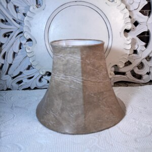 May include: A beige lampshade with a light brown and white marbled pattern. The lampshade is shaped like a bell and has a smooth, textured surface.