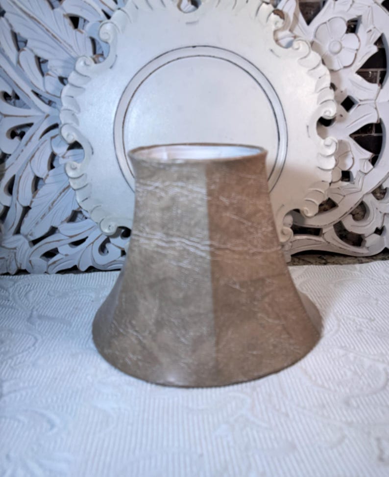 May include: A beige lampshade with a light brown and white marbled pattern. The lampshade is shaped like a bell and has a smooth, textured surface.