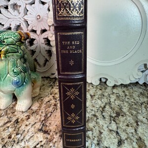 May include: A hardcover book titled "The Red and the Black" by Stendhal. The book has a dark brown leather cover with gold embossed decorative patterns and lettering. The spine features the title and author's name.