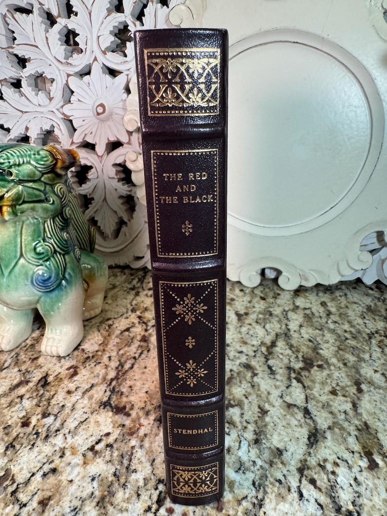 May include: A hardcover book titled "The Red and the Black" by Stendhal. The book has a dark brown leather cover with gold embossed decorative patterns and lettering. The spine features the title and author's name.