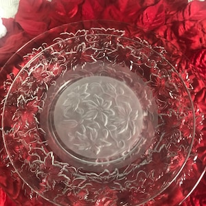 May include: Clear glass serving plates with a floral design. The plates have a frosted center and a detailed floral pattern around the edges. The plates are on a red background with red leaves.