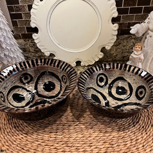 May include: Two brown ceramic bowls with black and white abstract designs. The bowls are on a woven straw placemat.