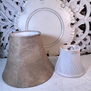 May include: Two lampshades, one is a larger beige shade with a textured surface and the other is a smaller white shade with a pleated design.