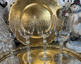 May include: Set of four clear glass wine glasses with etched leaf designs. The glasses are on a gold tray with a gold charger plate in the background.