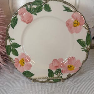 May include: A white ceramic plate with a scalloped edge features a floral design of pink roses and green leaves.