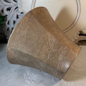 May include: A brown, textured, ceramic planter with a wide, flared opening. The planter has a distressed, aged look.