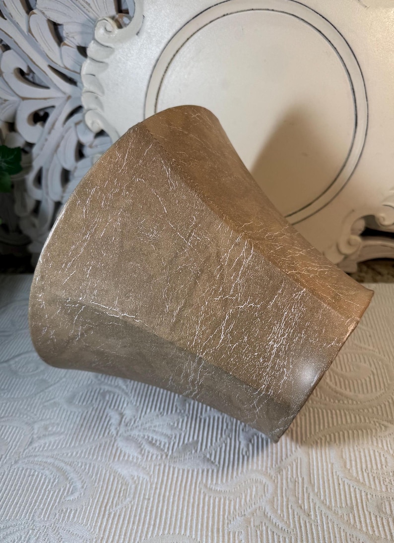 May include: A brown, textured, ceramic planter with a wide, flared opening. The planter has a distressed, aged look.
