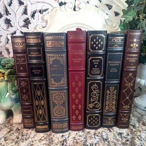 May include: A collection of antique books with decorative gold lettering and designs on the spines. The books are in various colors, including burgundy, black, and brown. Titles include "Anna Karenina" and "Wuthering Heights."