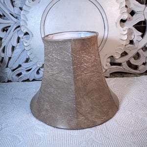 May include: A beige lampshade with a textured fabric. The lampshade is shaped like a bell and has a white lining.