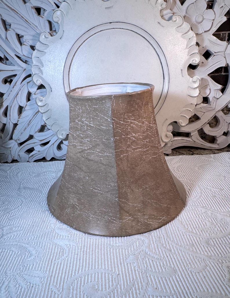 May include: A beige lampshade with a textured fabric. The lampshade is shaped like a bell and has a white lining.