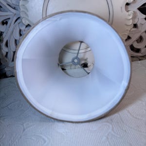 May include: A white lampshade with a beige fabric exterior. The lampshade is round and has a metal frame inside.