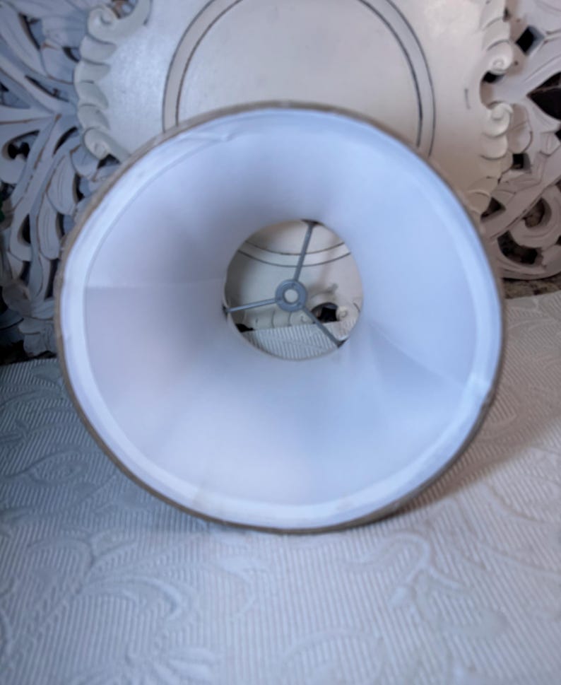 May include: A white lampshade with a beige fabric exterior. The lampshade is round and has a metal frame inside.