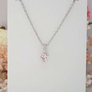 May include: A silver-toned necklace featuring a delicate chain and a single round, clear, faceted stone pendant. The pendant is suspended from a small, vertical bail that is embellished with tiny, sparkling clear stones for added detail.
