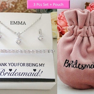 May include: A jewelry set featuring a silver-toned necklace, two earrings, and a tennis bracelet with clear stones. The display card reads EMMA and THANK YOU FOR BEING MY Bridesmaid!. A pink velvet drawstring pouch is labeled with Bridesmaid.