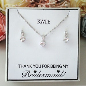 May include: A silver-toned necklace and earring set featuring clear round stones on a white display card. The card displays the text KATE and THANK YOU FOR BEING MY Bridesmaid! with two small black heart icons between the words.
