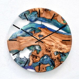 May include: Circular wall clock with a distinctive design, combining wood and resin. The clock face features natural wood tones and blue and green resin. Black clock hands and markers are included. The clock is approximately 30 cm in diameter.
