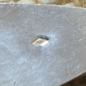 May include: Close-up of a silver-coloured metal surface with a small diamond-shaped mark.