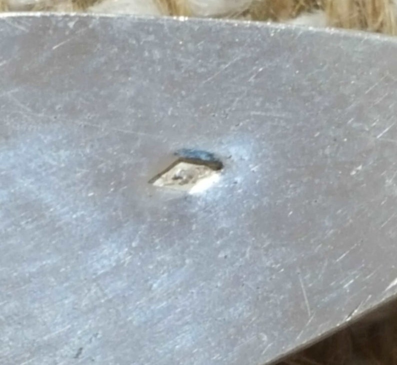 May include: Close-up of a silver-coloured metal surface with a small diamond-shaped mark.