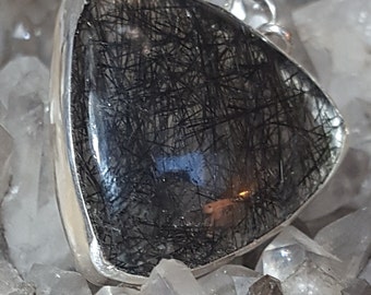 May include: A silver pendant featuring a triangular piece of black tourmaline with a clear quartz background. The pendant is surrounded by white quartz crystals.