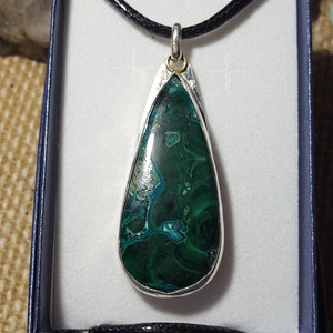 May include: A teardrop-shaped pendant necklace with a green and blue gemstone set in a silver bezel. The pendant is on a black cord.
