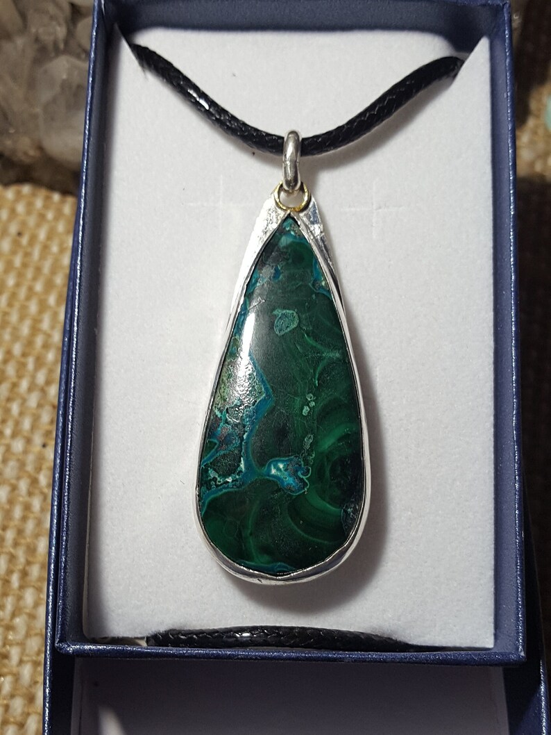 May include: A teardrop-shaped pendant necklace with a green and blue gemstone set in a silver bezel. The pendant is on a black cord.