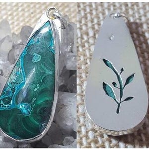 May include: A teardrop-shaped pendant featuring a green and blue chrysocolla stone set in silver. The reverse of the pendant is silver with a cut-out design of a leafy branch.