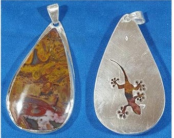 May include: A silver pendant with a teardrop shape. One side features a brown and red agate stone, the other side has a cut-out design of a gecko.