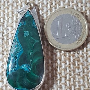 May include: A teardrop-shaped pendant with a green and blue gemstone set in silver. The pendant is about the size of a Euro coin.