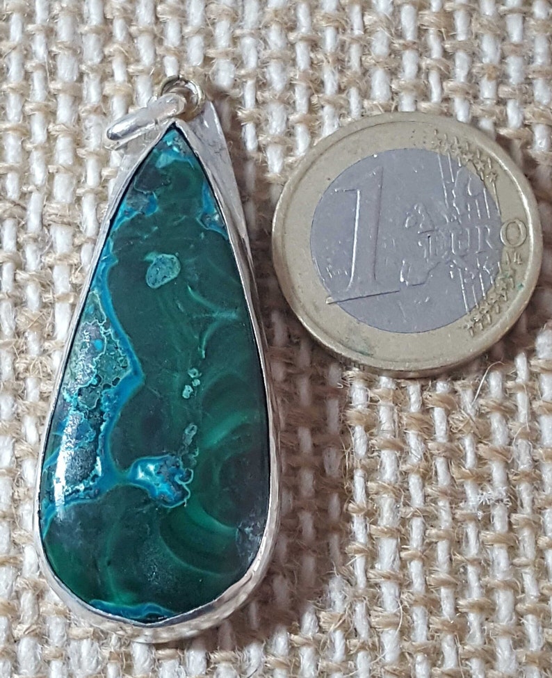 May include: A teardrop-shaped pendant with a green and blue gemstone set in silver. The pendant is about the size of a Euro coin.
