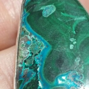 May include: A teardrop-shaped pendant featuring a green and blue malachite stone set in silver.