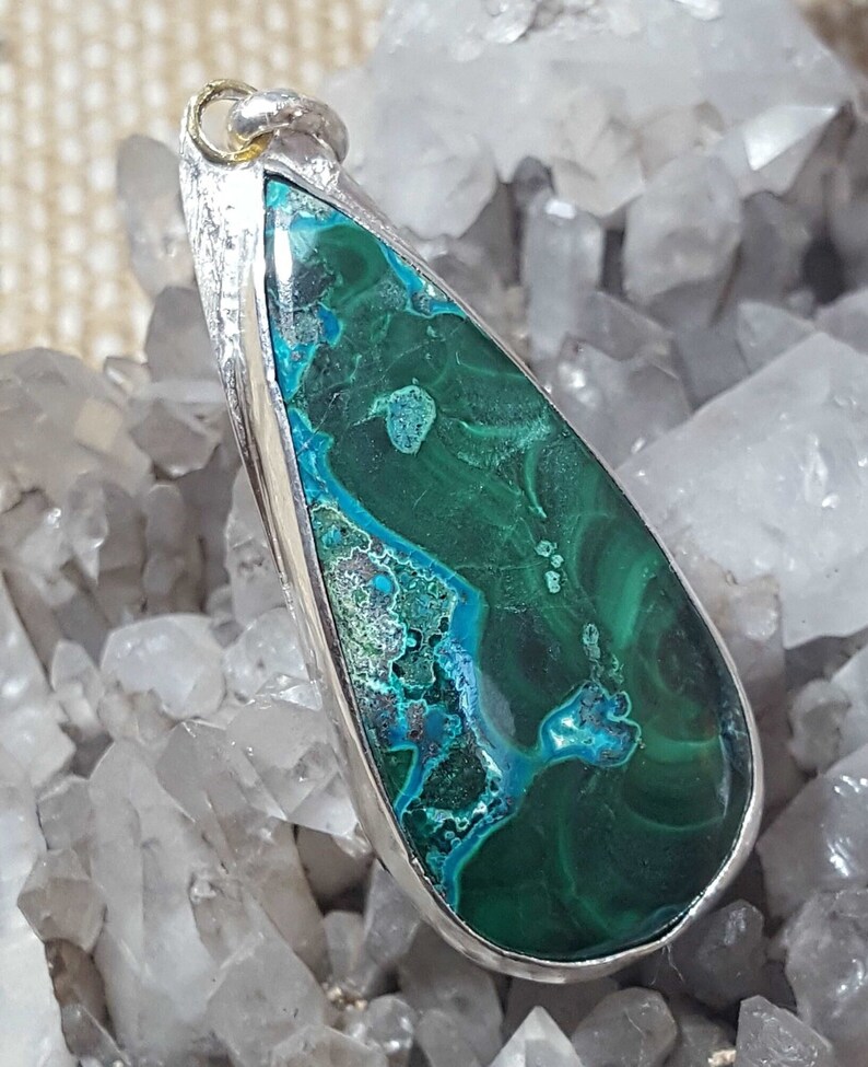 May include: A teardrop-shaped pendant featuring a green and blue gemstone set in silver. The gemstone has a swirling pattern of green, blue, and white.