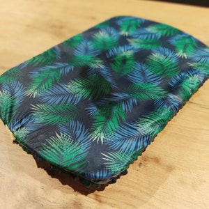 Peut inclure: Un film alimentaire rectangulaire avec un fond bleu foncé et un motif de feuilles de palmier vertes et bleues. Les bords du film sont légèrement froissés. Conçu pour couvrir les aliments.